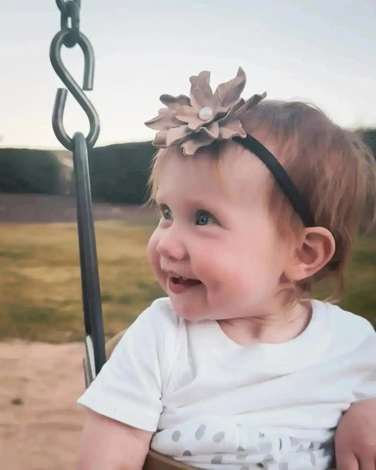 A little girl wearing a beautiful leather lace hair bow + headband w/ a pearl.