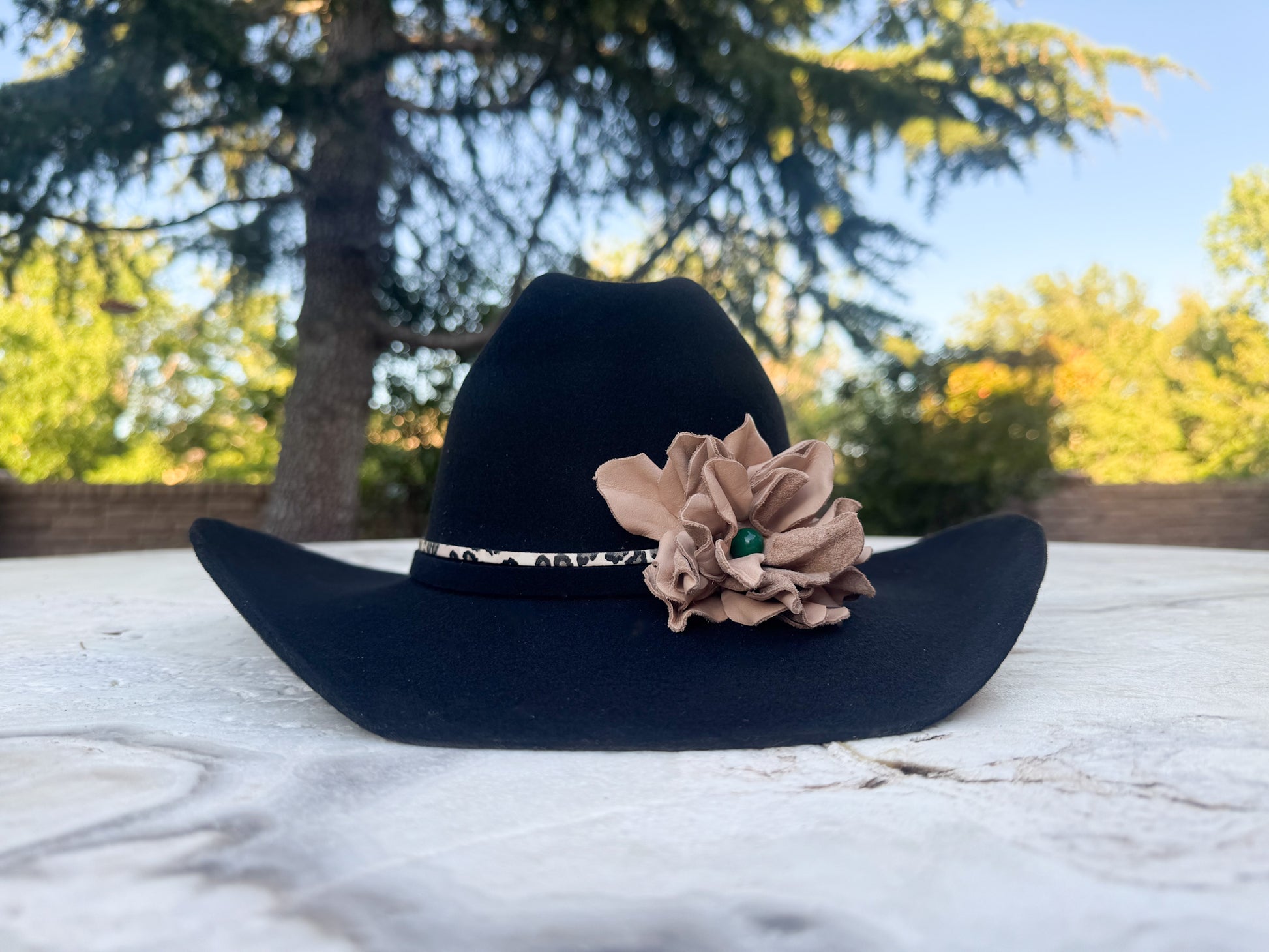 Black Cowgirl Hat w/ Leather Flower & Green Agate Stone Hat Band | Victoria | Westside Cowgirl. The hat is on a marble surface with a blurred natural background