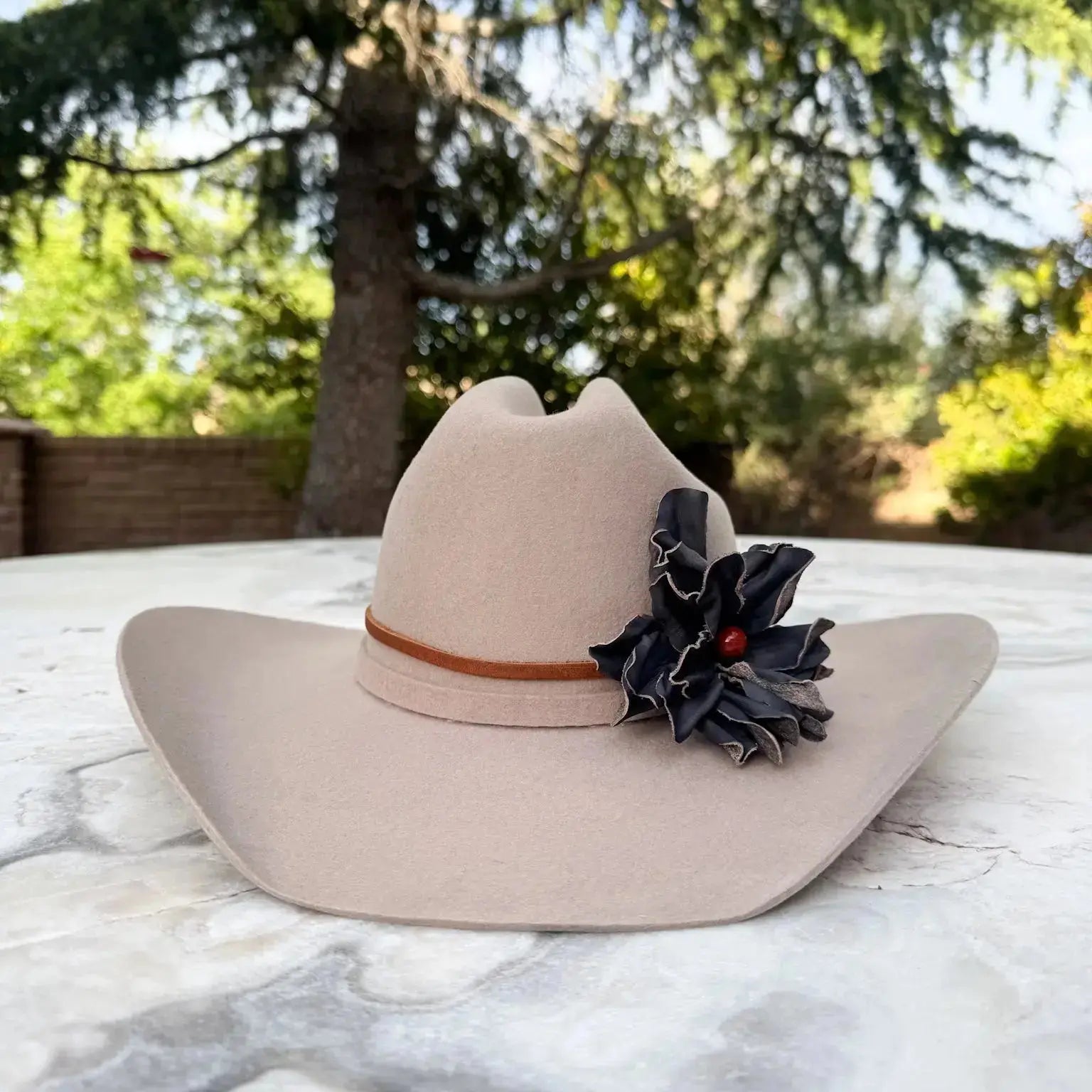 Cowgirl Hat w/ Black Leather Flower Red Jasper Stone Hat Band on a stone table with nature in the background.