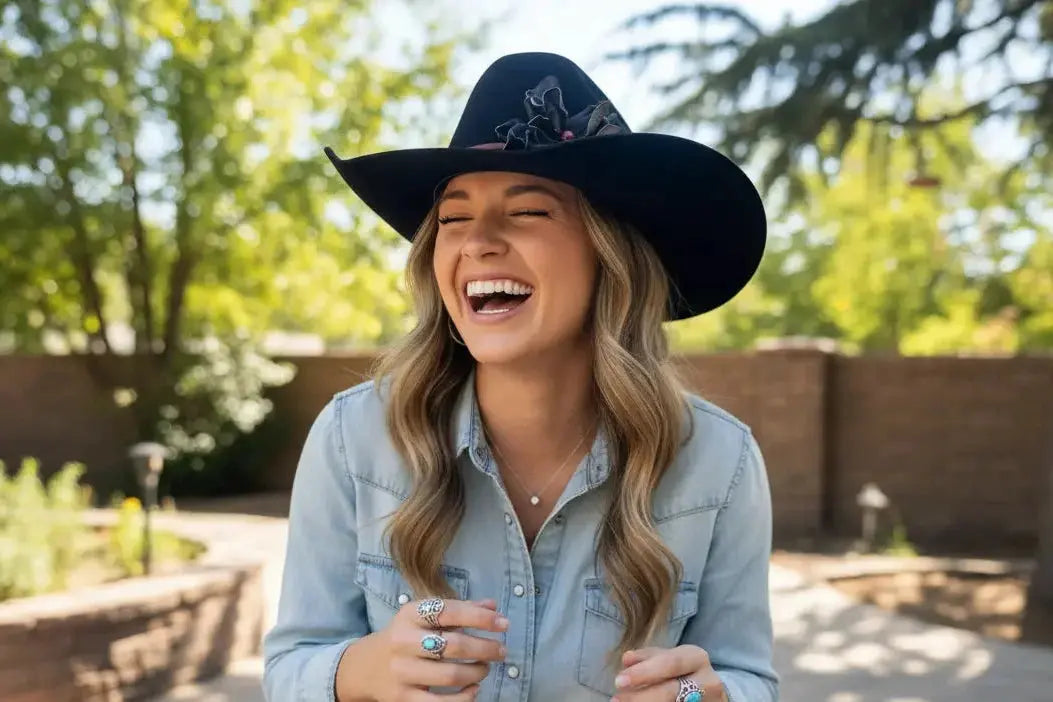 Woman wearing a black cowgirl hat with a black leather flower hat band and denim shirt outdoors